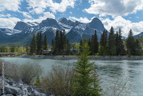 Stunning summer landscape of the Canadian Rocky Mountains and a calm river in Canmore, Alberta. Near Banff National Park with towering mountain peaks, Three Sisters. 