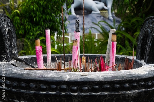 Traditional incense sticks and large burning pink joss sticks in a black stone ritual burner pot in a temple garden