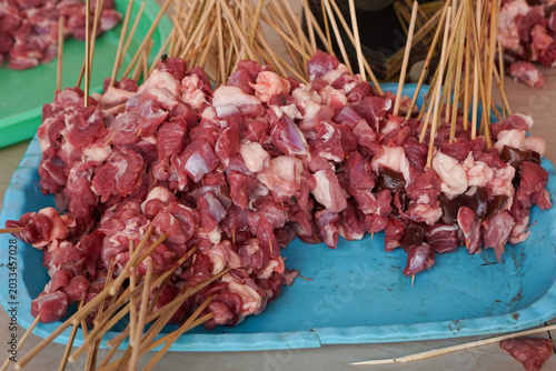 Raw meat skewers sit on a bright blue tray. Wooden sticks hold chunks of fresh, uncooked meat. Red and white marbling indicates freshness and quality