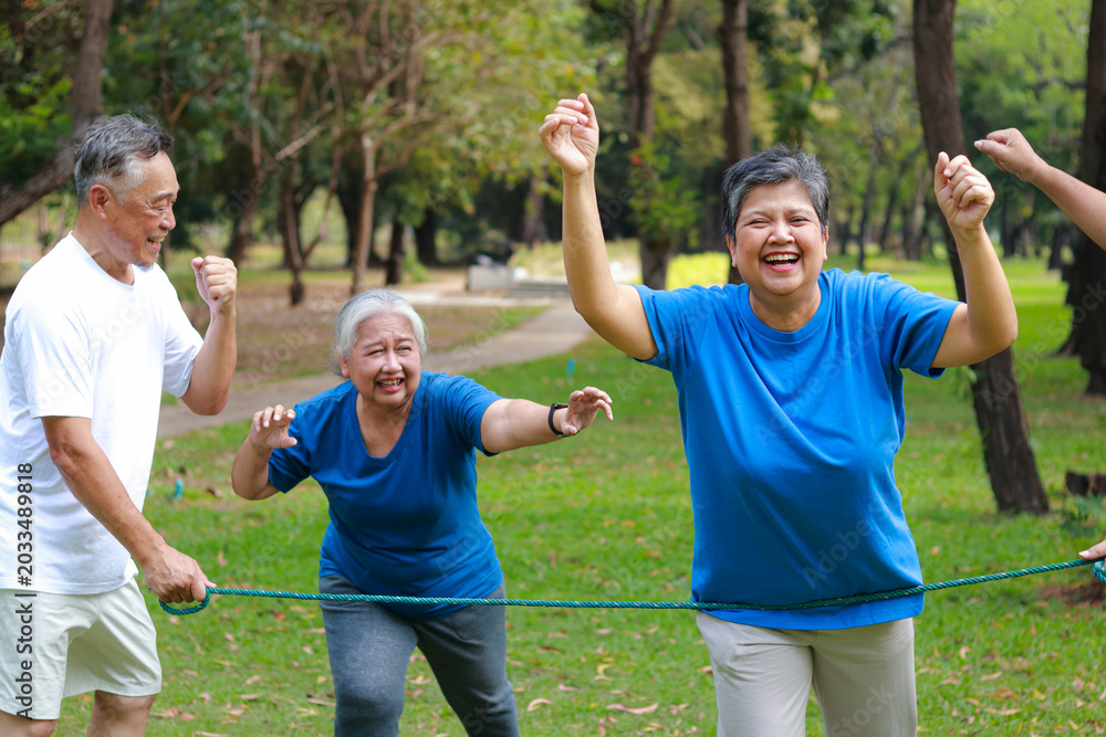 Obraz premium Happy Asian senior group running to finish line in park. Active elderly people enjoying outdoor exercise for healthy lifestyle and retirement wellness.