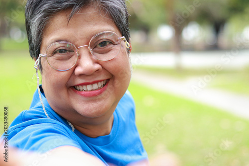 Close-up portrait of smiling senior Asian woman with glasses and happy eyes outdoors. Health care in retirement