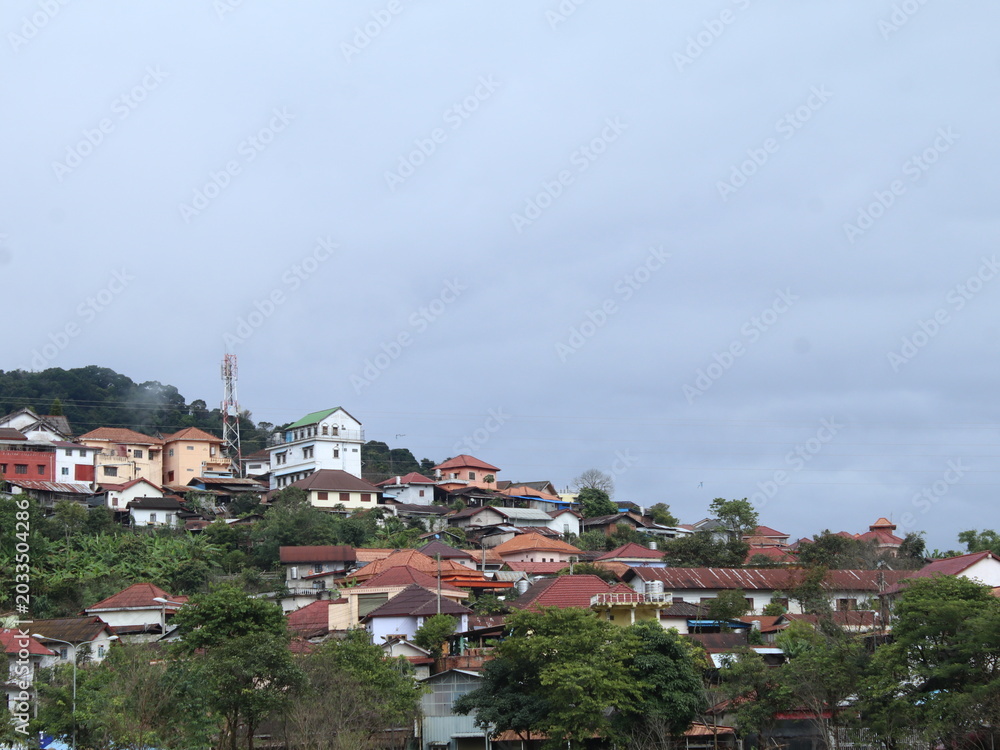 Fototapeta premium Hillside Town with Orange Tiled Roof Houses and Telecommunication Tower Under Cloudy Sky in Rural Laos