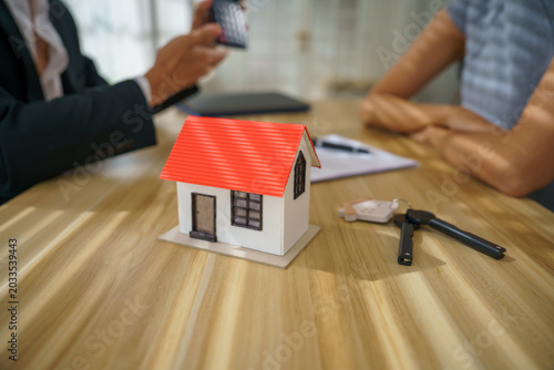 Real estate house model red roof key contract mortgage agreement agent buyer seller on wooden table during meeting about deal discussion under warm light conveys trust and optimism
