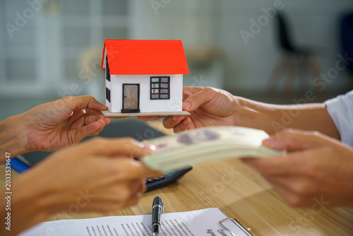 Real estate house purchase sale contract money payment mortgage loan agreement scene, hands exchange cash for model home, paperwork and pen on table in office, indoor, during closing deal