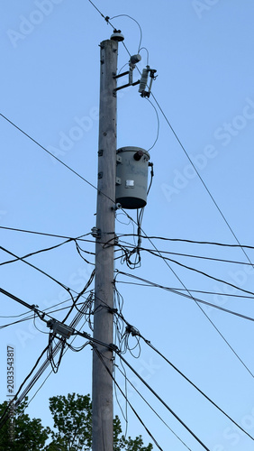 A wooden utility pole and transformer with power lines against a clear blue sky