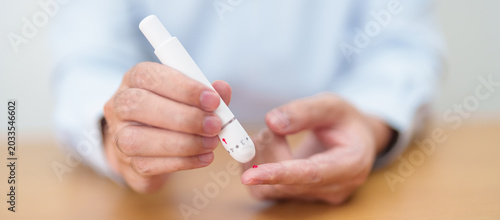 Foto Hand using lancet pen on finger with Blood drop glucose testing or Diabetes checking by digital blood glucose meter
