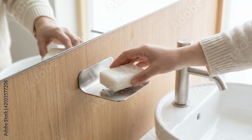A hand selecting a fresh bar of soap from a modern bathroom holder, emphasizing daily hygiene