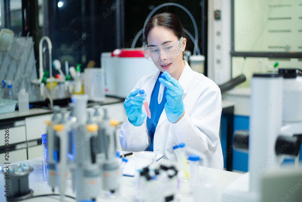 Fototapeta premium Young Asian scientist analyzing samples with microscope in a modern laboratory, focusing on medical research, biotechnology, healthcare, and innovation.