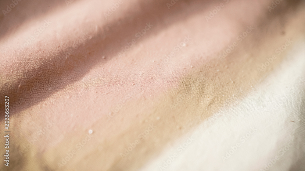 Fototapeta premium Golden sunlight illuminating the subtle blush to creamy beige gradient of woven fabric