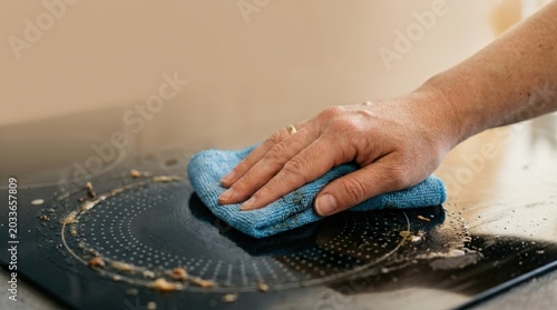 Hand cleaning kitchen stove surface with blue sponge and soapy water. Kitchen cleaning involves removing grease and dirt from stove surface with sponge.