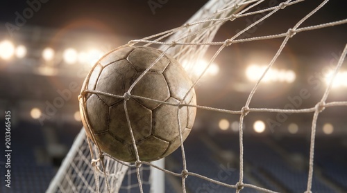 A vintage soccer ball perfectly caught in the back of the net, illuminated by the vibrant stadium lights, signifying a decisive goal and the thrilling moment of victory in an evening match