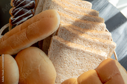 Close-up of sliced whole wheat toast and fresh bakery buns in a wicker basket