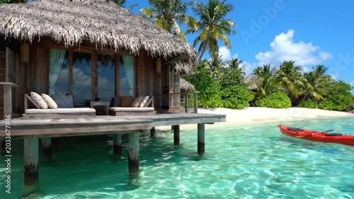 Tropical overwater bungalow with thatched roof and wooden dock in turquoise ocean with red kayak island paradise resort luxury vacation island paradise resort luxury vacation