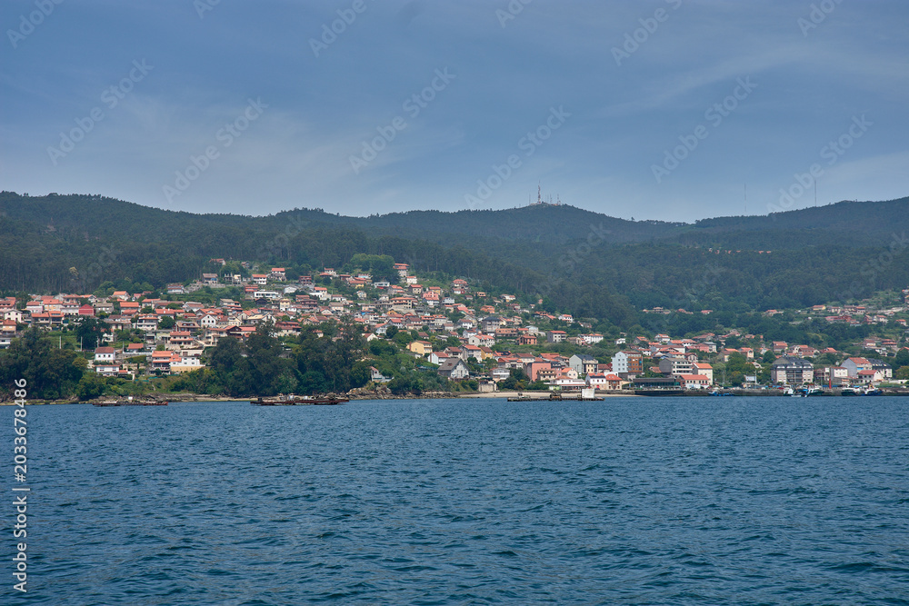 Fototapeta premium Small coastal houses integrated into the green landscape of the Vigo estuary, photographed from the sea