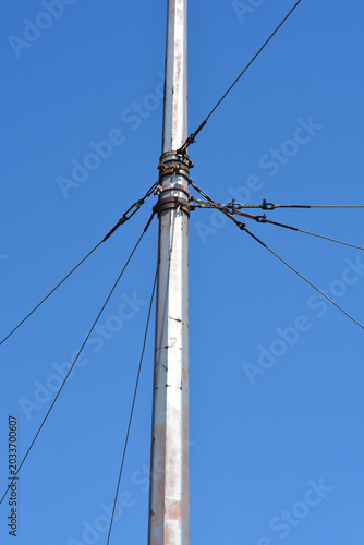 A detailed close up view of a metal tram line utility pole with steel guy wires and tensioners against a clear blue sky