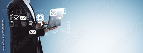 Businessperson using laptop with holographic checkmarks and email icons for d...