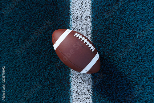 American football ball lying on textured turf field with white line, showing ...