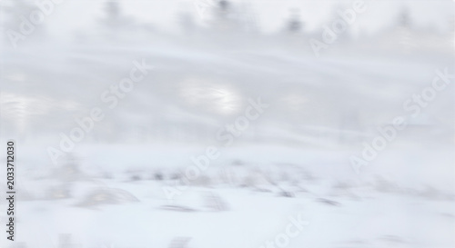 Motion blurred view of a snowy landscape with dark pine trees and a small building seen from a moving vehicle during a winter storm