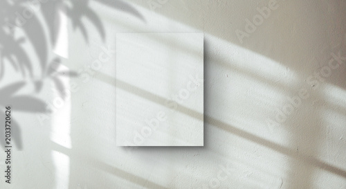 A blank paper mockup on a textured wall with soft tropical leaf shadows and natural light.