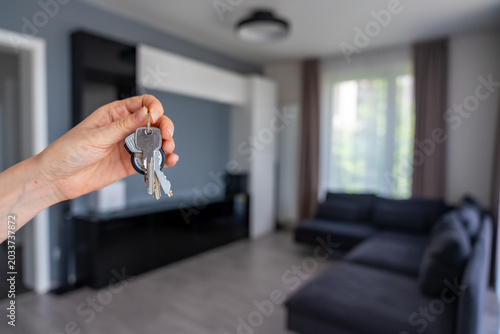 Hand holding apartment keys in furnished resale apartment living room interior. Secondary housing purchase and existing property ownership concept