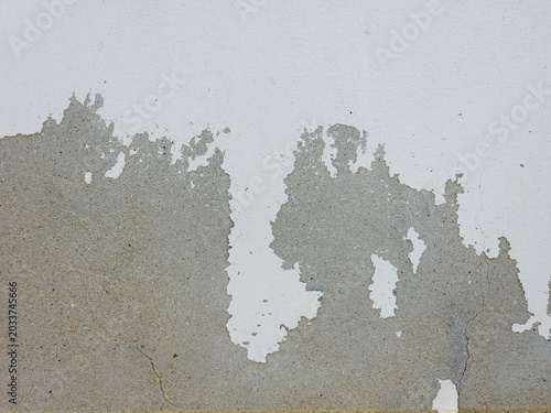 Peeling white paint reveals the rough grey concrete surface of an old weathered wall.