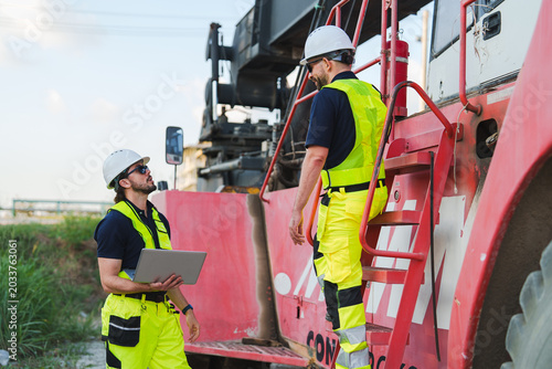 Construction worker team beside heavy machine at industrial site safety helmet safety vest engineer laborer machinery inspection communication teamwork outdoors