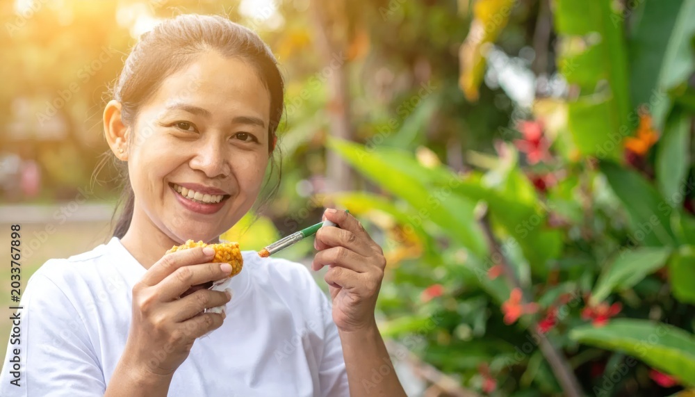 Fototapeta premium Smiling Asian Woman Eating Grilled Corn in Tropical Garden