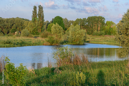 Fotografia This is a peaceful landscape featuring a calm blue river winding through lush green meadows