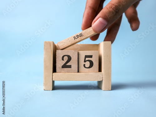 Schilderij op canvas A woman's hand holds a wooden block with June written on it on a wooden block calendar for June twenty-fifth against a light blue background