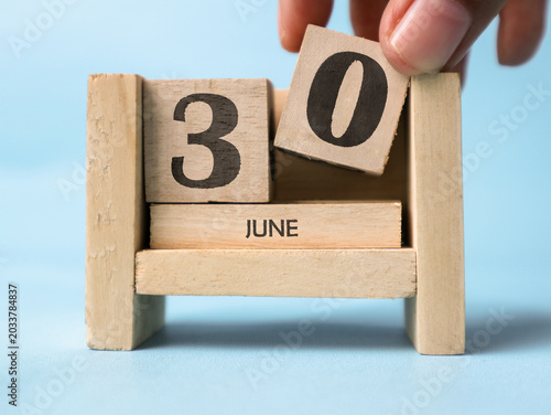 Tableau sur toile A woman's hand is holding a wooden block with the number zero written on it on a wooden block calendar for June thirtieth on a light blue background