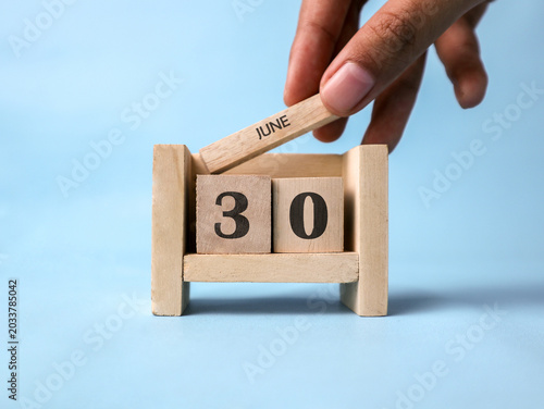Fotografi A woman's hand holds a wooden block with June written on it on a wooden block calendar for June thirtieth against a light blue background