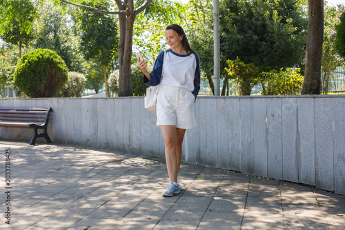 Foto Pretty woman with smartphone walking on city street