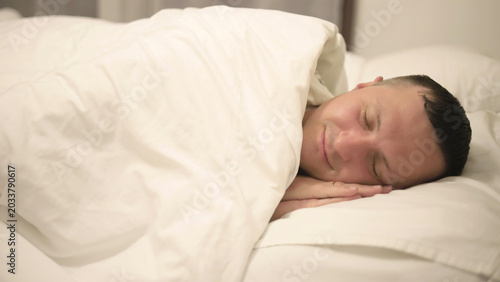 Schilderij op canvas A man sleeps sweetly and peacefully on a pillow under a blanket in a white bed in the bedroom