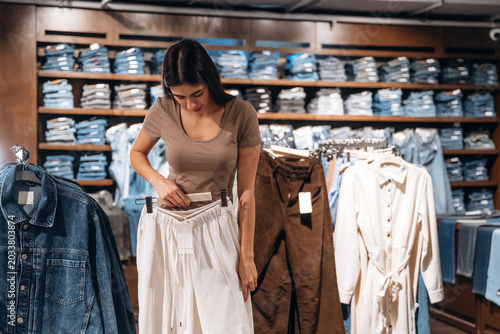 фотографія Female shopper examining white pants while standing in a clothing store with she