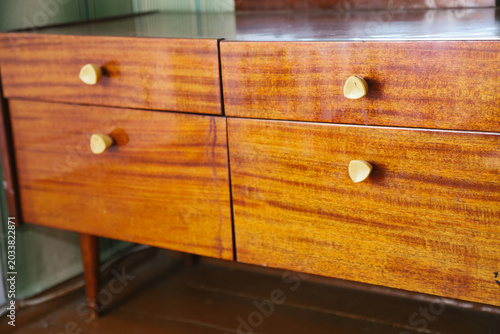 Wooden dresser with four drawers and golden knobs. The surface has a rich, warm finish, showcasing the natural grain of the wood.