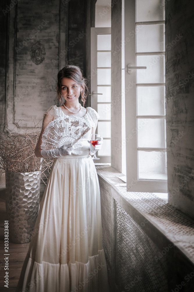 Obraz premium Elegant woman in vintage white gown by window in classic interior
