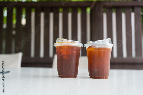 Two iced black coffee in clear plastic cups with lids on table