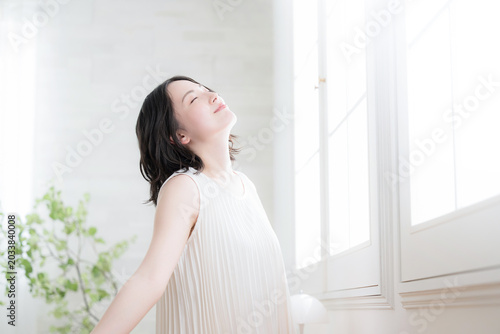 Foto 窓辺で朝の光を浴びながら深呼吸の伸びをする女性の健康ライフスタイルイメージ