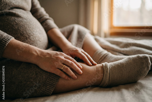 Pregnant woman gently massaging her swollen ankle while sitting indoors  