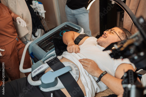 Fotografie Overweight middle aged male client undergoing a noninvasive electromagnetic muscle stimulation treatment on the abdomen at an aesthetic clinic