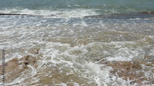 The warm, turbid waves of the Indian Ocean lap against a rocky slab on the shore, a scene from the nature of Sri Lanka