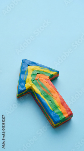 Plasticine clay rainbow arrow pointing up on blue background