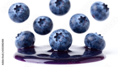Close-up of fresh ripe blueberries floating above glossy blueberry juice on a white background, vivid deep blue and purple tones