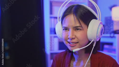Excited young Asian girl playing online computer game with headset and microphone at home, esports and live streaming concept.
