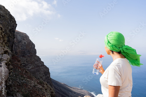 Foto Woman in green headscarf hydrating with a water bottle, admiring the vast ocean
