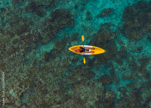 Aerial top view of a woman relaxing on a yellow kayak over a beautiful coral reef in crystal clear turquoise sea water.