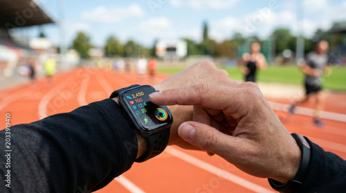 A close-up of a male athlete's wrist checking a smartwatch during a workout on an athletic track.