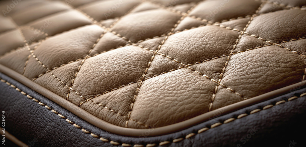 Fototapeta premium Close-up of quilted brown leather upholstery with diamond stitching and textured seams in warm light.