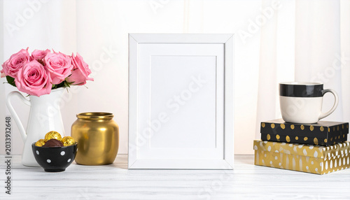 Pink Roses and Cherished Memories: A charming display featuring a bouquet of delicate pink roses in a white pitcher, a golden decorative jar, a small bowl of chocolates, an empty white picture frame.
