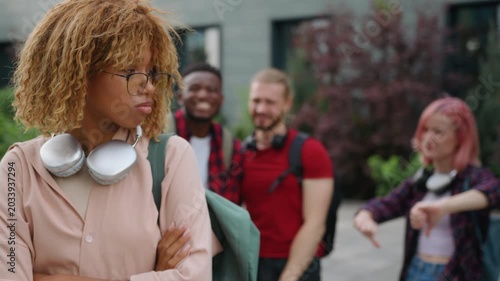 Stressed African American student girl woman suffering with bullying in high school college academy university in city outdoors classmates multiracial students bully mocking laughing discriminate